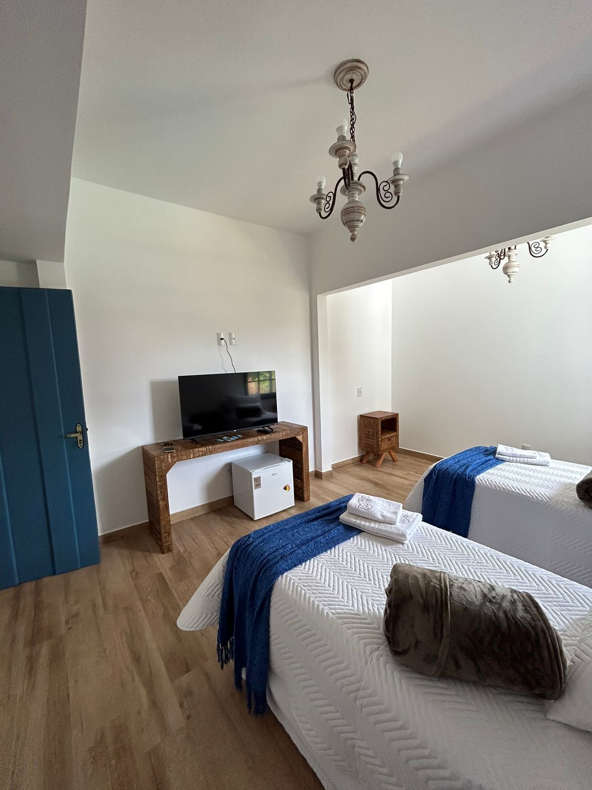 A hotel room with two beds, a television, a small refrigerator, and a wooden side table.