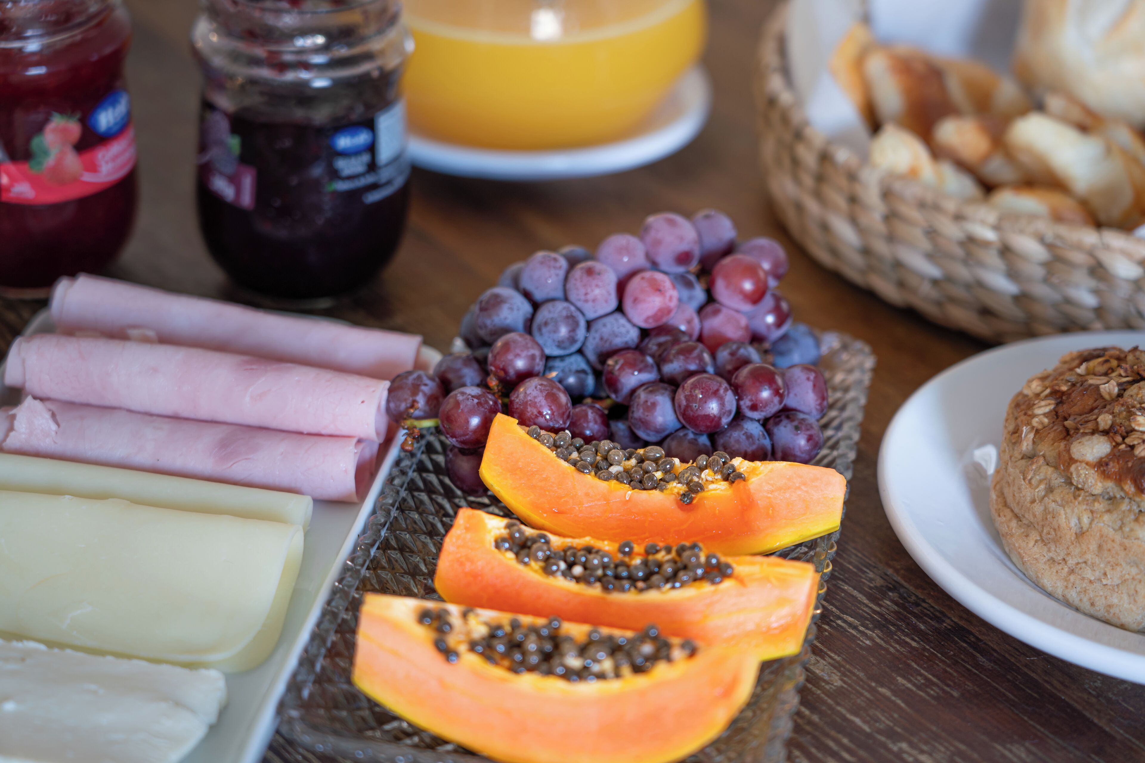 Una mesa con diversos alimentos, como jamón en rodajas, queso, uvas y una cesta de pan.