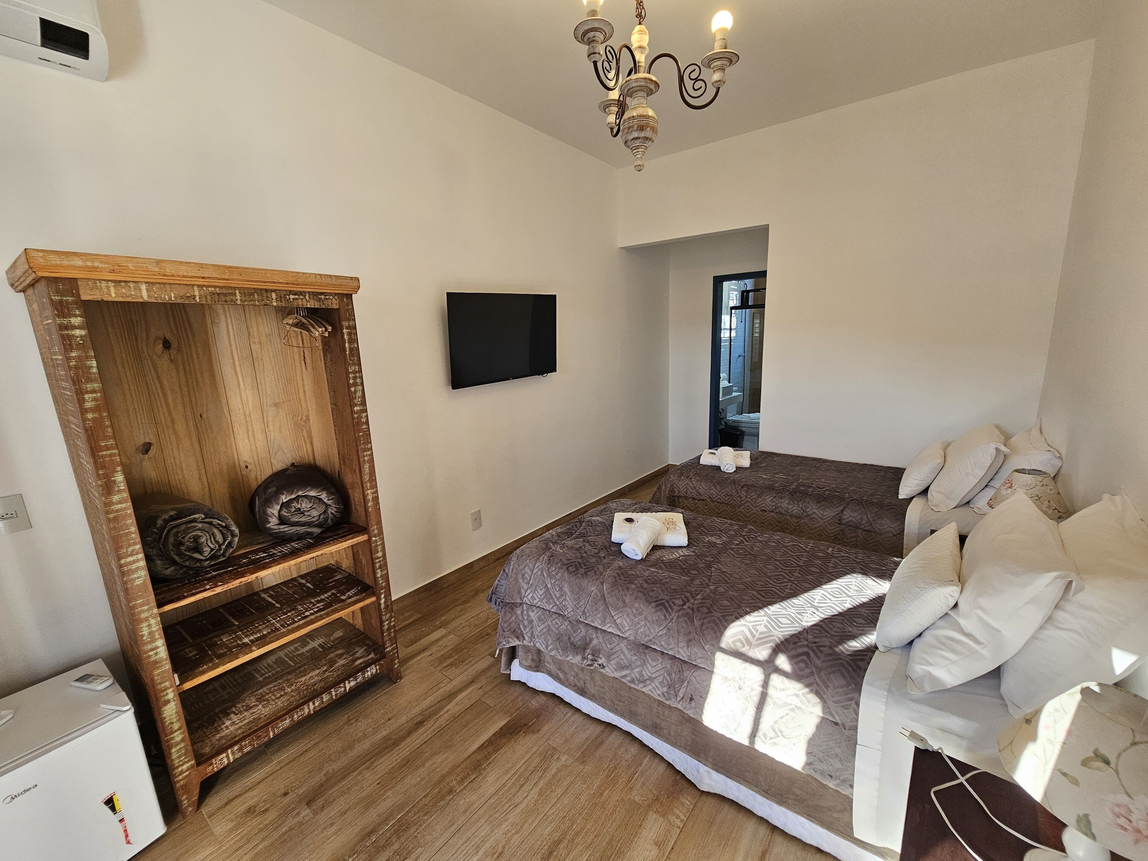 A bedroom with a wooden wardrobe, a bed with patterned bedding, a flat-screen TV, and a chandelier.