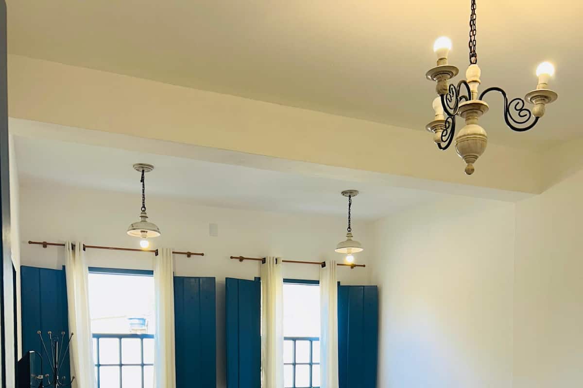 A hotel room with two beds, a desk, and a chair. There are curtains on the windows, and a chandelier hangs from the ceiling.