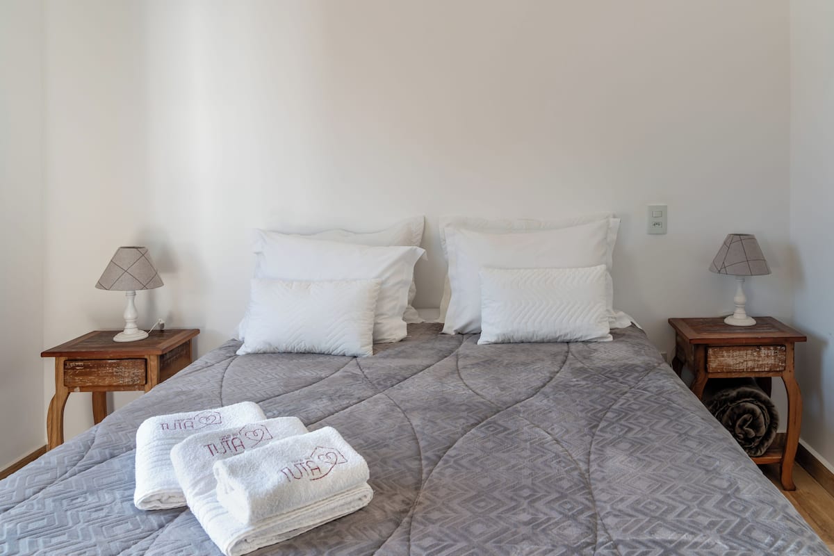 A neatly made bed with a patterned bedspread, two pillows, two bedside lamps, and three folded towels on the bed.