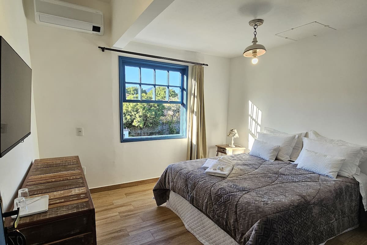 A bedroom with a bed, a wooden dresser, a TV, and a window with curtains.