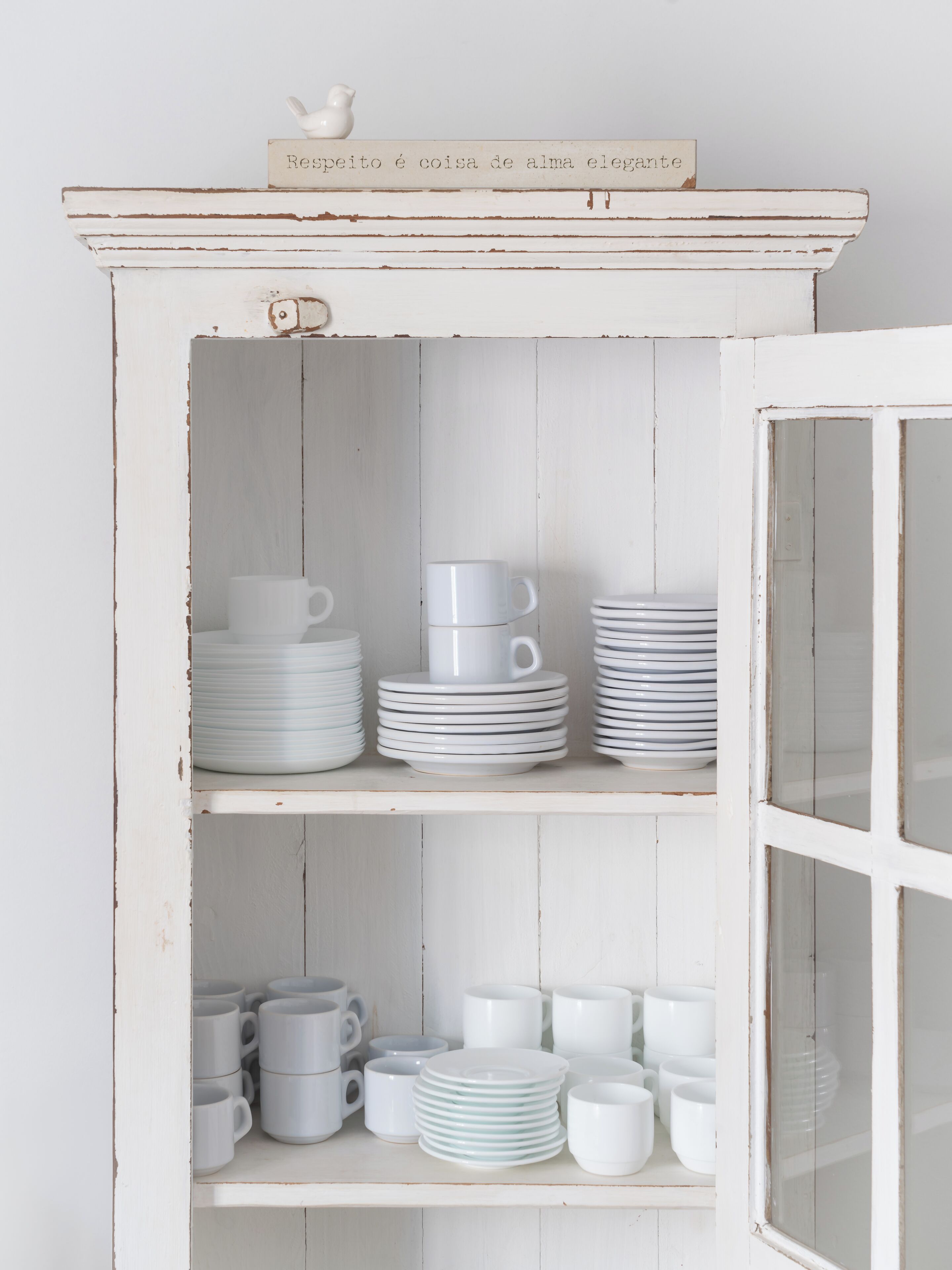 A white wooden cabinet with multiple shelves holding stacks of white plates and cups.