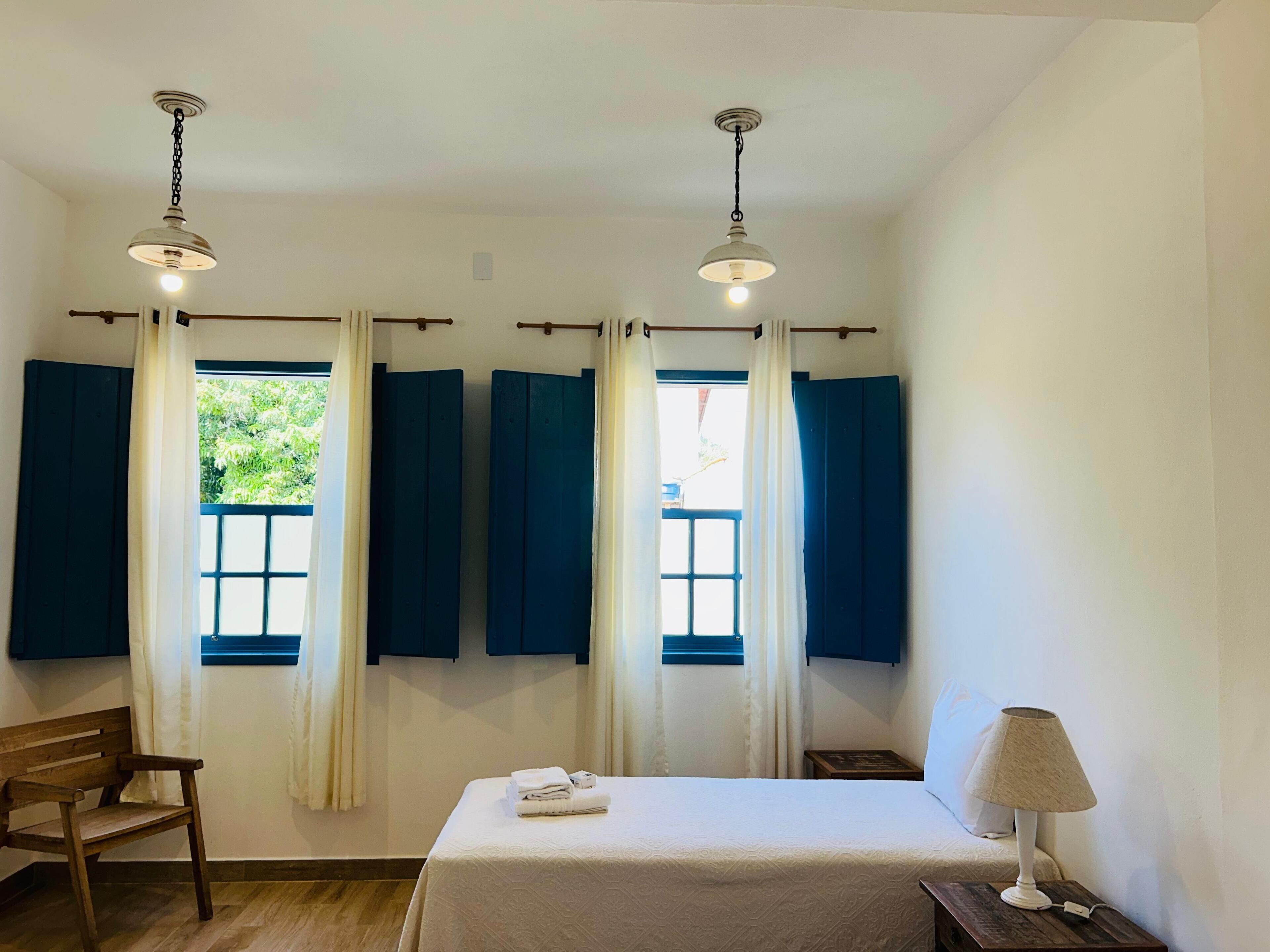 A room with a bed, a desk, and two windows with curtains.