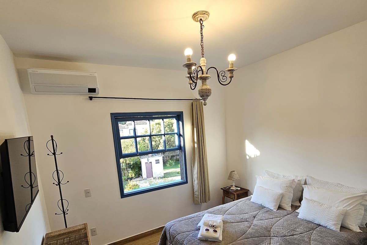 A bedroom with a bed, a window, a chandelier, and a wooden dresser.