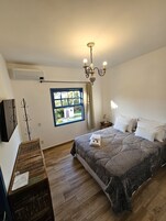 A bedroom with a bed, a window, a chandelier, and a wooden dresser.