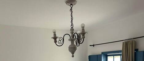 A bedroom with a bed, a nightstand, a lamp, a window with curtains, and a chandelier.