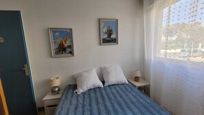 A bedroom with a bed, two pillows, a nightstand with a lamp, and two framed pictures on the wall. - Appartement Avec vue Mer à Marseillan Plage (Marseillan)