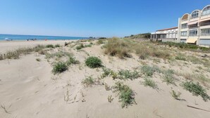 A beach with sparse vegetation and a building with multiple balconies. - Appartement Avec vue Mer à Marseillan Plage (Marseillan)