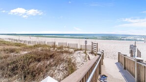A beach with a wooden walkway leading to the shore, a sandy beach, and a clear blue sky.