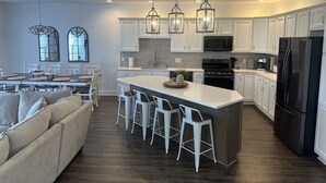 A modern kitchen with white cabinetry, a central island with bar stools, a large refrigerator, and pendant lighting. - NEWLY BUILT condo - premium features, game room, firepit, short walk to village (Ellicottville)