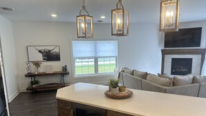 A modern kitchen with wooden cabinets, a central island, pendant lighting, a large window with a view, and a fireplace. - NEWLY BUILT condo - premium features, game room, firepit, short walk to village (Ellicottville)