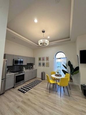 Een moderne keuken met grijze kastjes, roestvrijstalen apparatuur en een eethoek met gele stoelen.