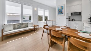A modern kitchen with white cabinets, a dining table set for four, and a large window overlooking a garden.