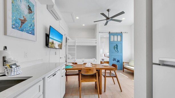 A modern kitchen with white cabinetry, a wooden dining table, and a blue door with seahorse decorations.