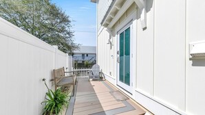A narrow deck with a wooden bench and a chair, a small potted plant, and a white fence.