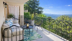 A balcony with a sofa, chairs, a table, and a view of a mountainous landscape.