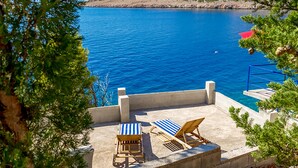 En kystterrasse med to liggestole og en pool, med udsigt over et klart, blåt hav.