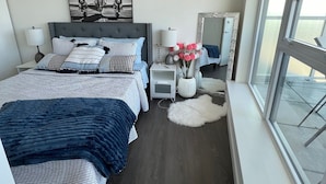 A modern bedroom with a large bed, bedside tables, a mirror, and a view through a window. - A Brand New Luxury apartment in Richmond,200 mts from Skytrain and Mall. (Richmond)