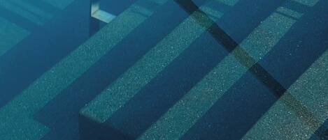 Vista subacuática de una piscina con agua azul cristalina y un trampolín.