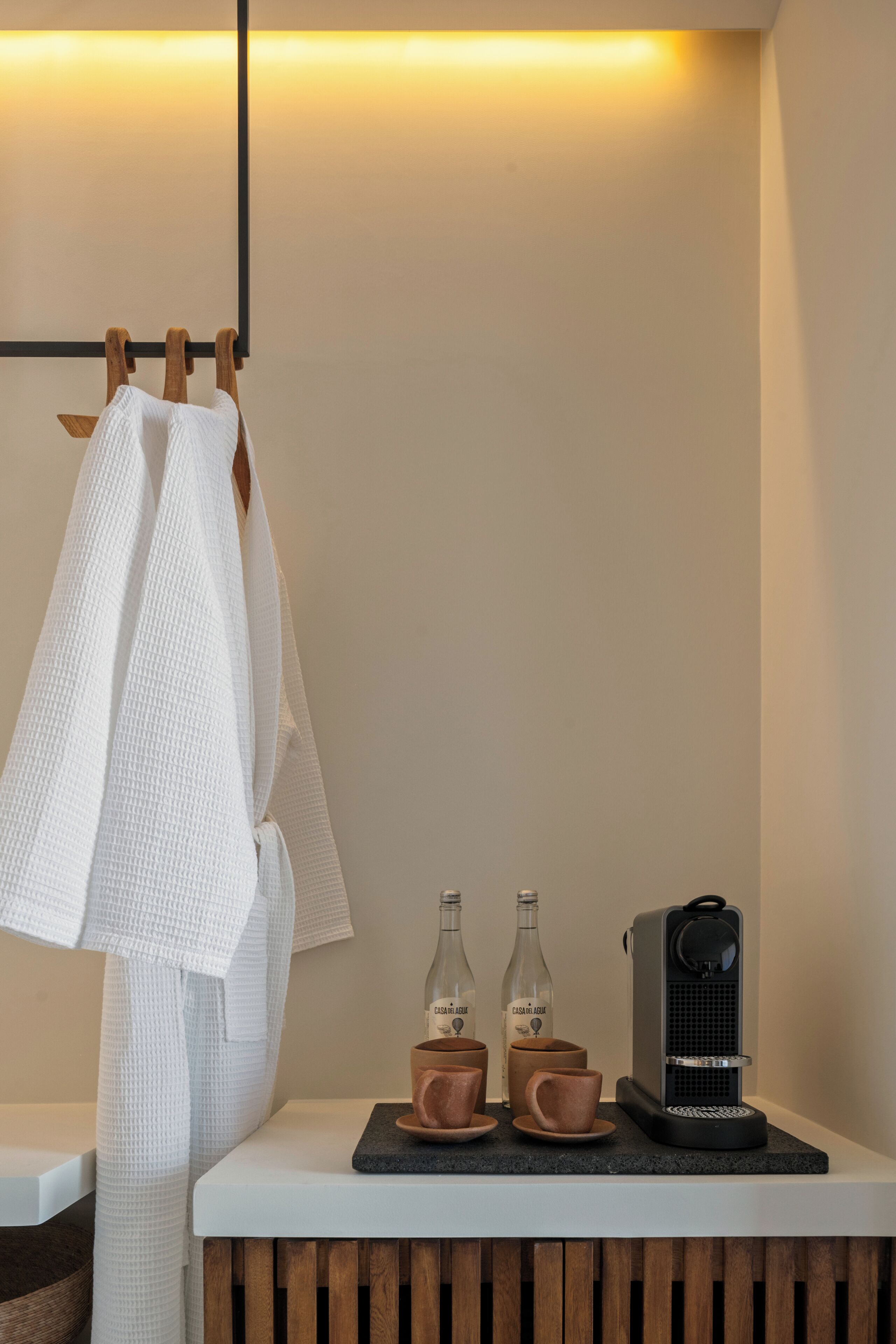 A bathroom with a towel rack, two bottles of water, and a coffee machine on a countertop.