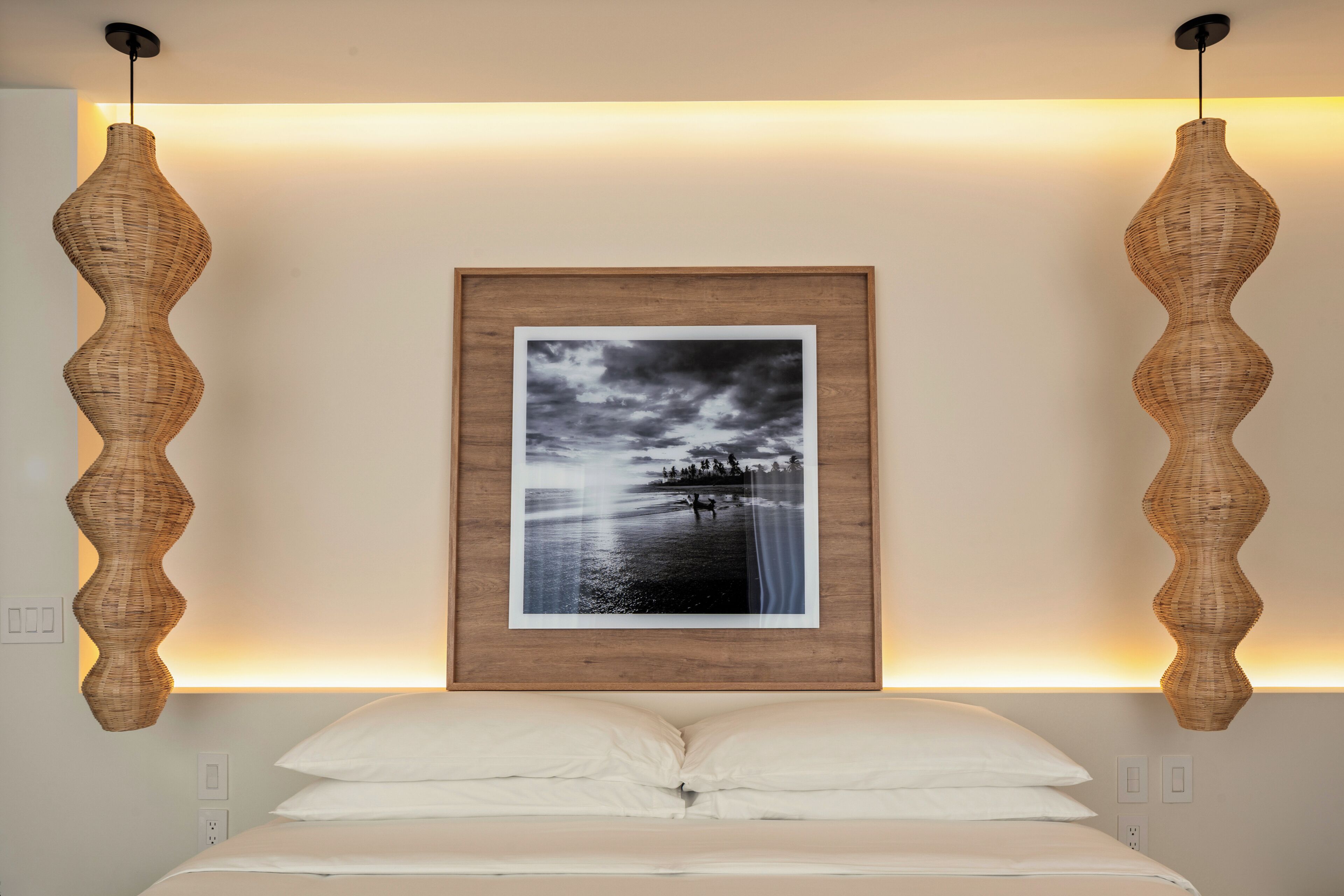 A bedroom with a bed, a framed photograph on the wall, and two wall-mounted lamps.
