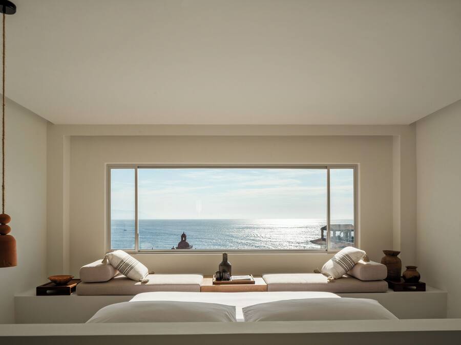 Un dormitorio con una ventana grande, una cama, una mesita de noche y una lámpara colgante.