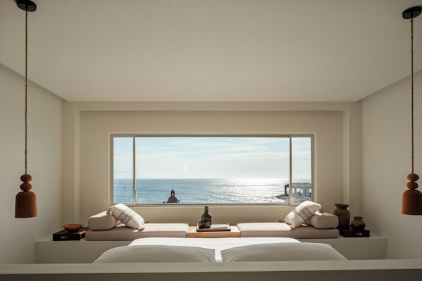 Un dormitorio con una ventana grande, una cama, una mesita de noche y una lámpara colgante.