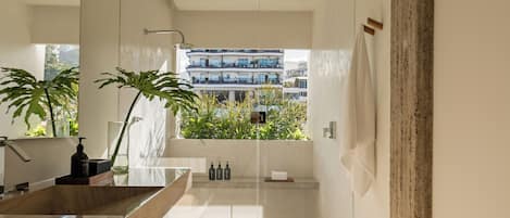 Un baño moderno con un espejo grande, un tocador de madera, un lavabo de mármol y vistas a un edificio con balcones.