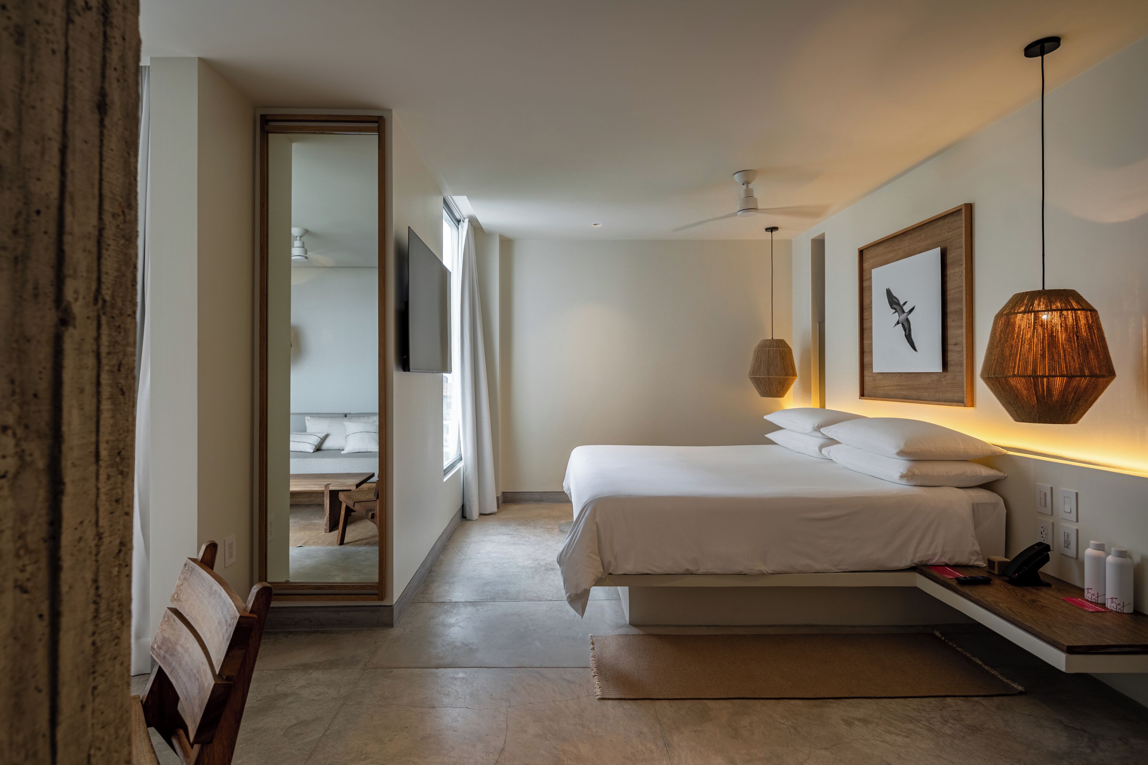 A modern bedroom with a bed, bedside table, and a view into another room.