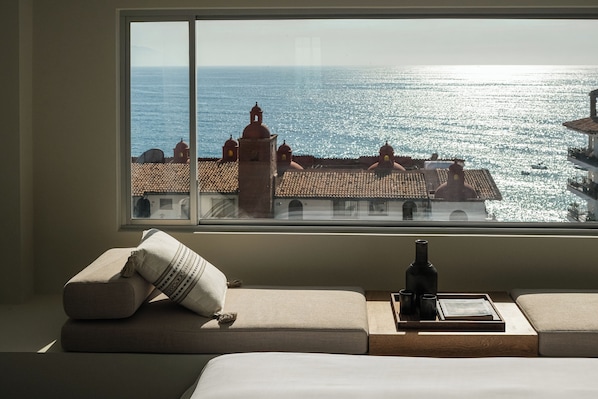 Una habitación con un ventanal grande que da a la vista costera, un sofá con cojines y una botella sobre una bandeja.