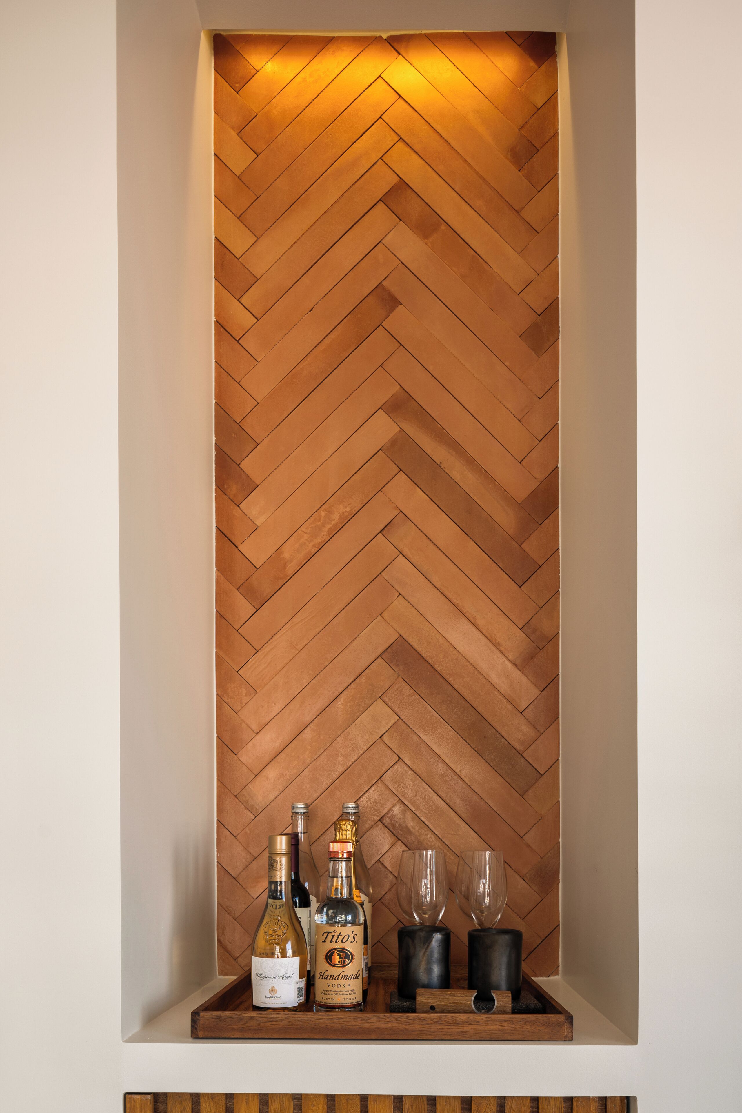 A wooden herringbone wall with a shelf containing bottles and glasses.