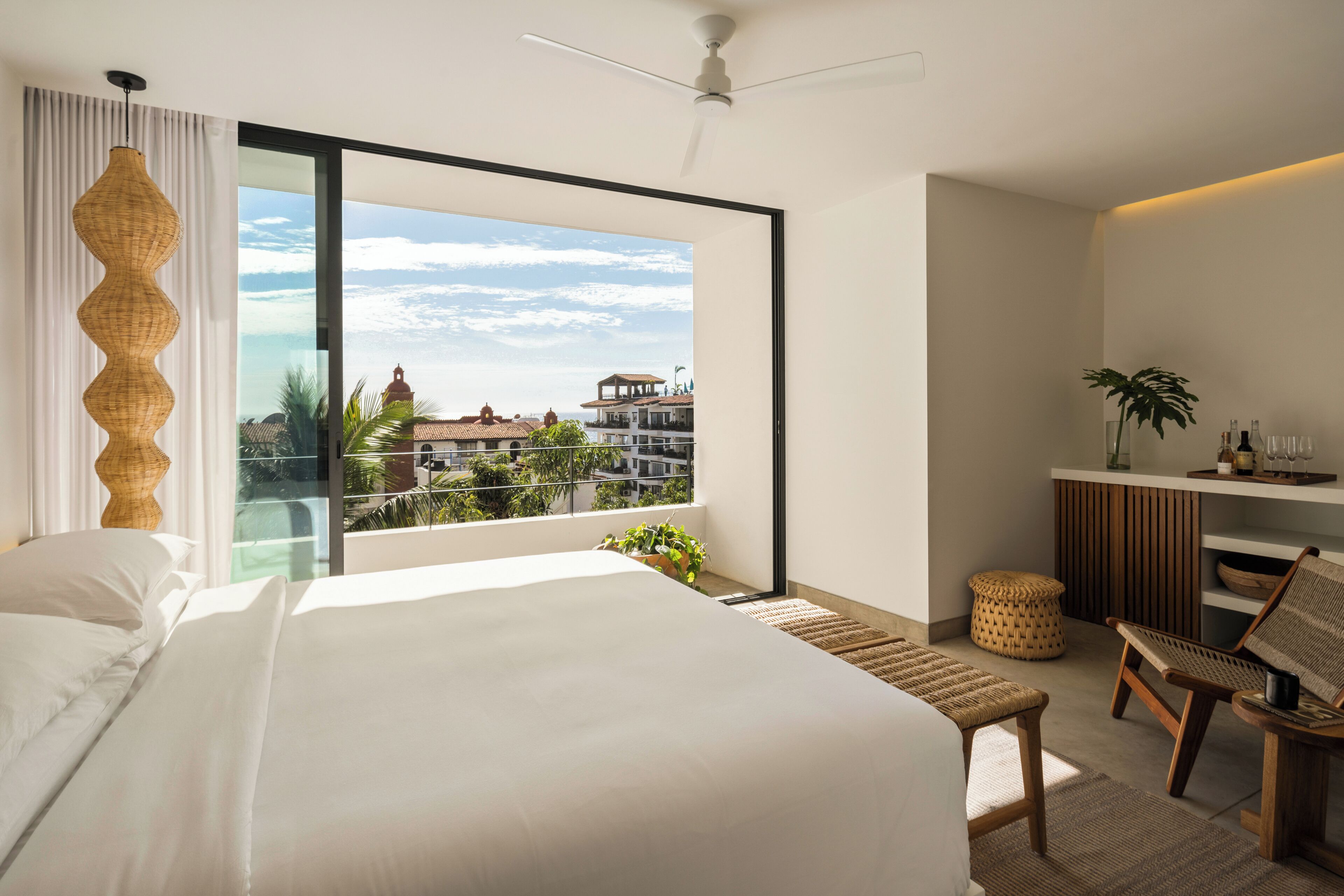 Une chambre d’hôtel moderne, dotée d’un grand lit, d’un bureau avec une chaise, d’une petite table et offrant une vue sur la ville grâce à une grande fenêtre.
