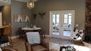 A dining area with a round table and chairs, a fireplace, and a view through glass doors to an outdoor seating area. - Luxury Mountain Home with Fireplace, Yosemite & Bass Lake (Oakhurst)