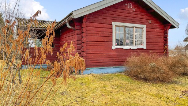 Une petite cabane en bois rouge, avec une fenêtre et un petit porche.