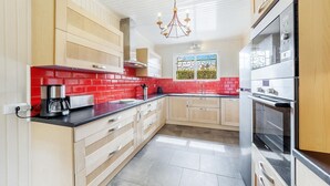 Une cuisine moderne avec des meubles en bois clair, un crédence en carreaux rouges, des appareils électroménagers en acier inoxydable et une fenêtre donnant sur un espace verdoyant.