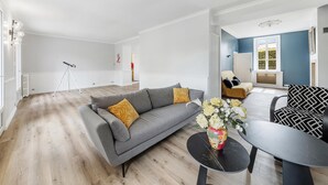 Un salon spacieux avec un canapé gris, une table ronde noire et un mur d’accent bleu.