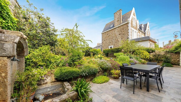 Un bâtiment en pierre doté d’un jardin et d’un patio aménagé avec une table et des chaises.