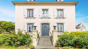 Un bâtiment à deux étages, doté d’une entrée centrale, flanqué de deux fenêtres avec volets, et d’une enseigne au-dessus de la porte.