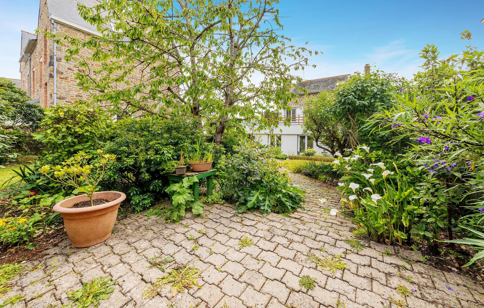 A garden pathway leading to a building with stone walls and a variety of plants and flowers.