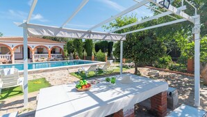 A poolside area with a pergola, a table with a basket of fruits, and lounge chairs. - Villa Cuqui Antequera by Ruralidays (Málaga)