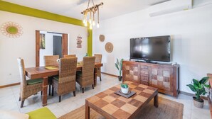 A dining area with wicker chairs, a wooden table, and a television on a cabinet. - Villa Cuqui Antequera by Ruralidays (Málaga)