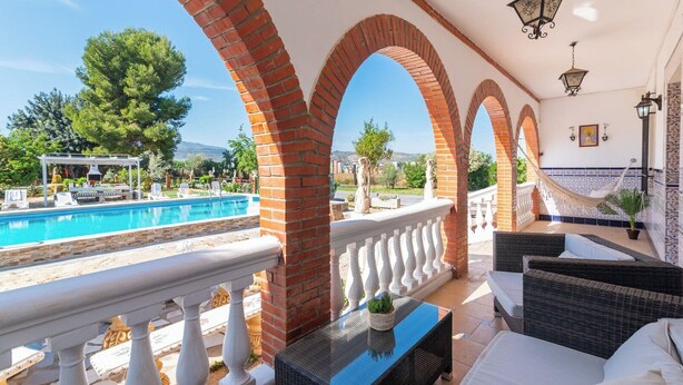 A balcony with a pool, white balustrades, wicker furniture, and a tiled wall with a patterned border. - Villa Cuqui Antequera by Ruralidays (Málaga)