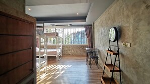 A room with a bunk bed, a wooden wardrobe, a round mirror on a stand, and a window with curtains. - Hi Samui Hostel (Koh Samui)