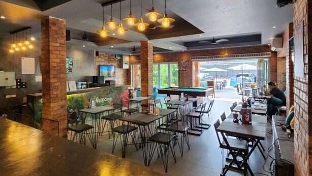 A restaurant with a bar area, tables, and chairs. There is a pool table and a person playing pool. - Hi Samui Hostel (Koh Samui)