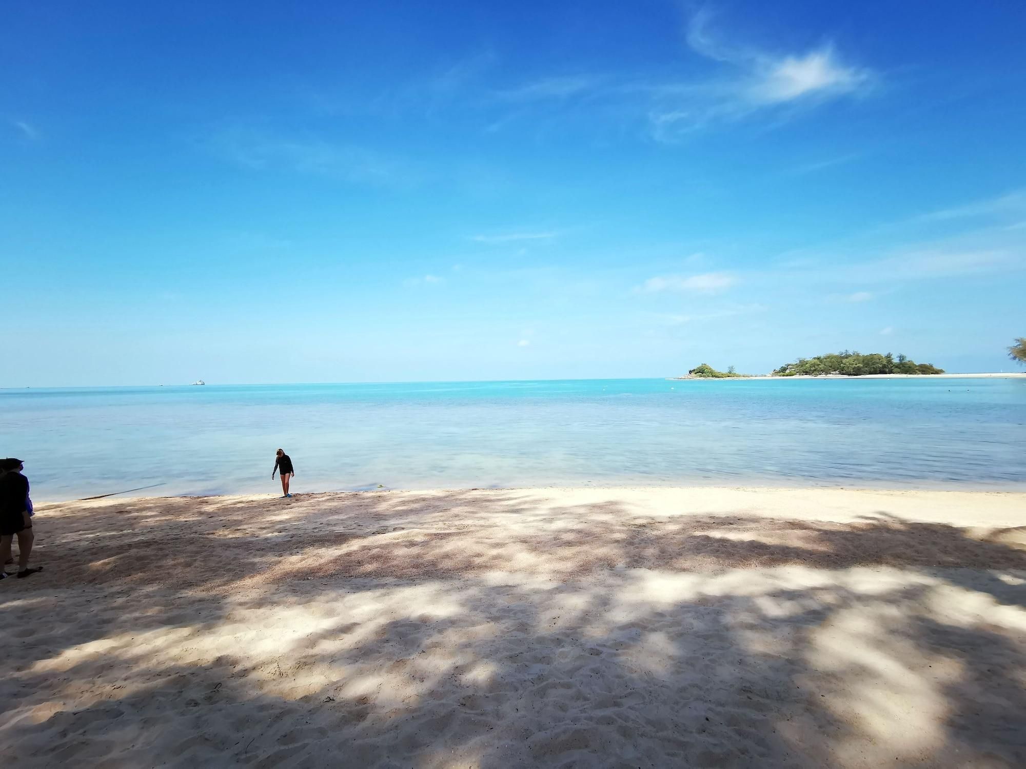 A beach with clear blue water, a person walking, and a small island in the distance.