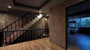 A modern interior with a wooden floor, a staircase with black railings, and a view of greenery outside. - Hi Samui Hostel (Koh Samui)