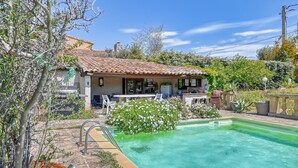 Una casa con techo de tejas, piscina y un patio con mobiliario exterior.