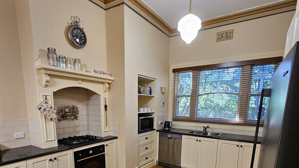 A kitchen with wooden flooring, white cabinets, a black refrigerator, and a window with blinds. - Ruston House - Port of Echuca (Echuca)