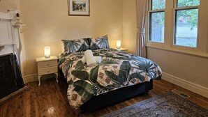 A bedroom with a bed, two bedside tables, a nightstand, a framed picture on the wall, and a window with curtains. - Ruston House - Port of Echuca (Echuca)